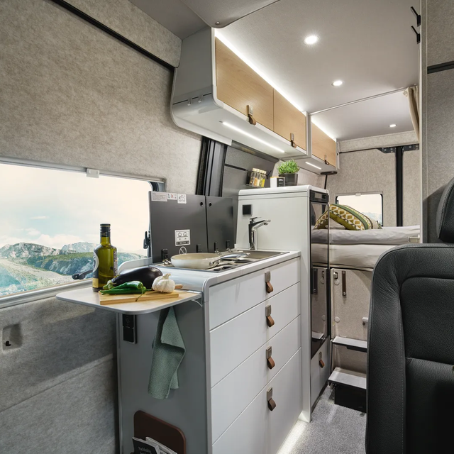 Sur l'extension de la cuisine du HYMER Grand Canyon S, il y a des légumes. En arrière-plan, la kitchenette avec cuisinière, évier et réfrigérateur est visible.