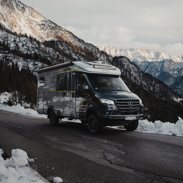 Off-road motorhome with neon green decals stands on a road in the mountains, trees and snow can be seen in the background
