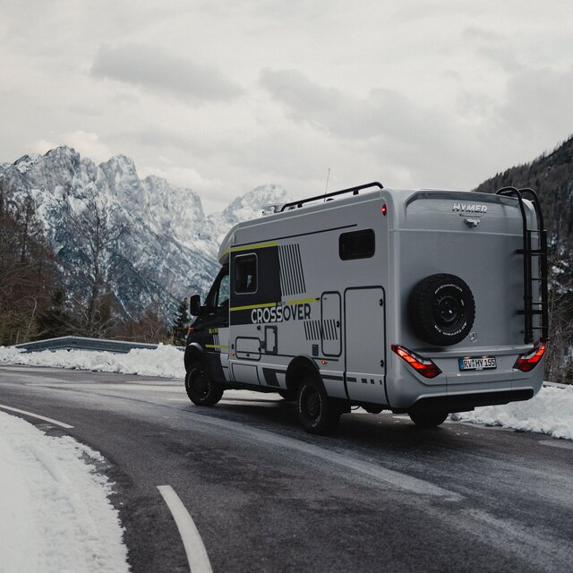 Off-road capable motorhome driving on a snowy road, snow-covered mountains can be seen in the background, side view of the vehicle