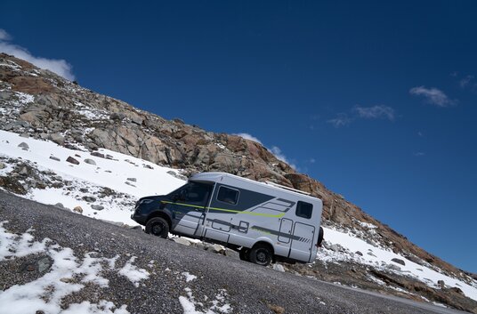 HYMER ML-T 570 Crossover 4x4 driving uphill on a road in a mountain landscape with some snow
