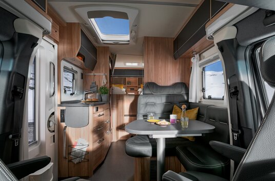 Living room in the HYMER ML-T CrossOver: seating area, laid table, panoramic roof vent, kitchen block, rear area with bedroom