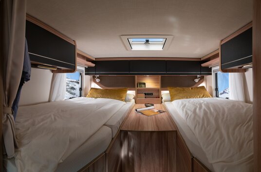 Covered lengthways single beds with yellow decorative pillows, central entry, overhead storage cupboards in the rear of the HYMER ML-T Crossover 570