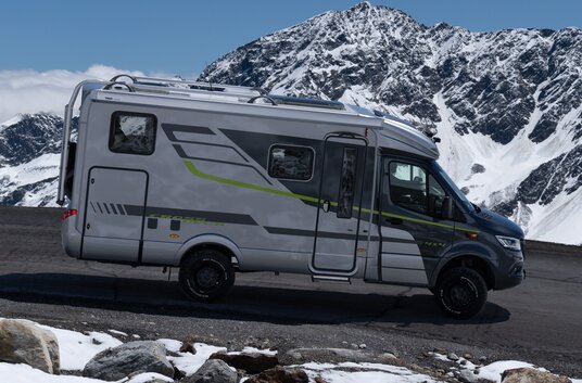 HYMER ML-T 570 Crossover 4x4 driving downhill on a road in a mountain landscape with some snow