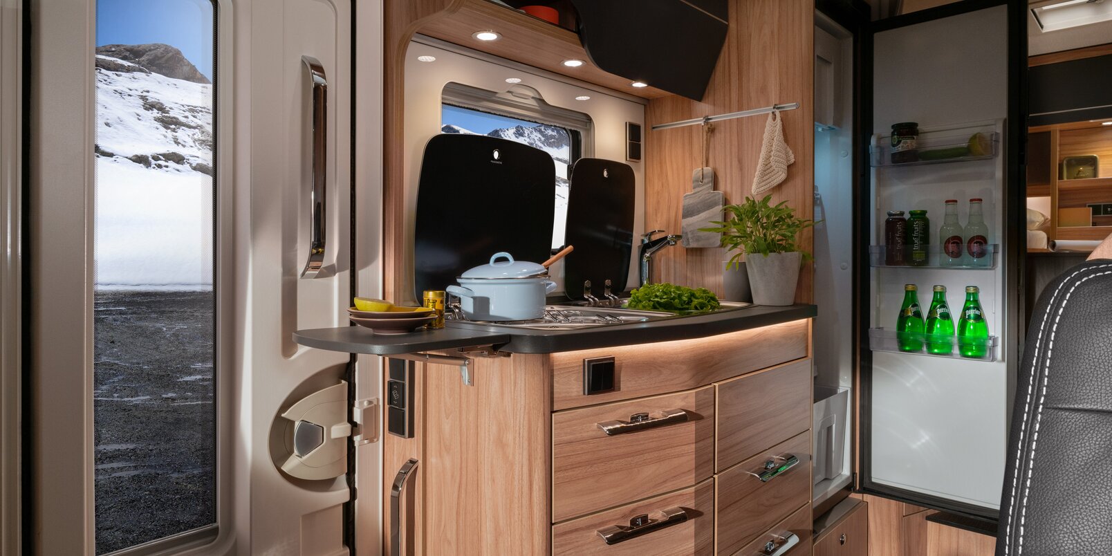Entrance door, kitchen block with utensils and worktop extension, open refrigerator in the HYMER ML-T 570 CrossOver