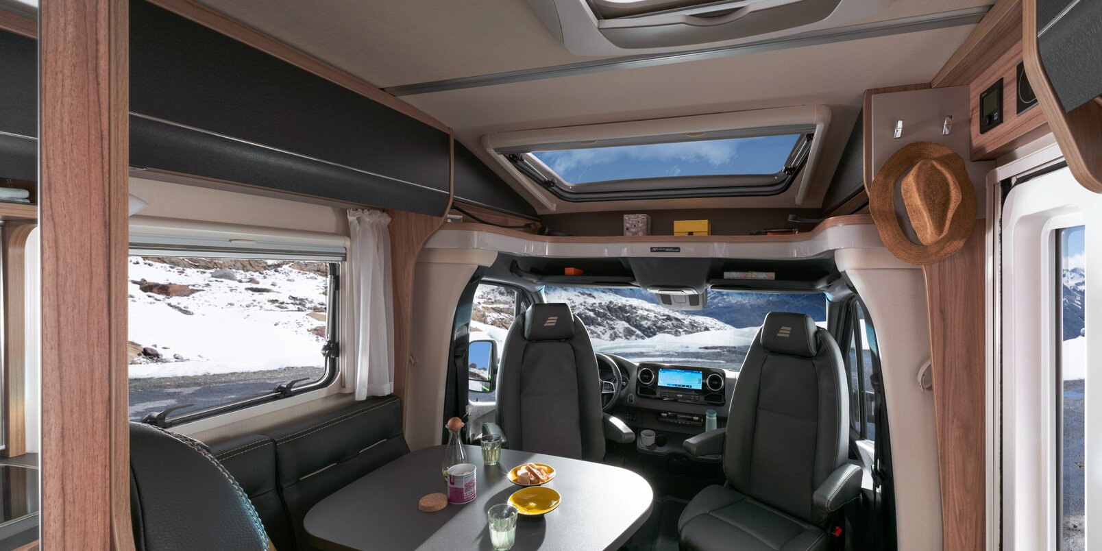 Living space in the HYMER ML-T CrossOver: dark leather seating area, laid table, panoramic roof vent, driver's seats and driver's cab