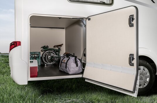 The HYMER motorhome's rear garage is open and loaded with a folding bike, water box and other items of luggage