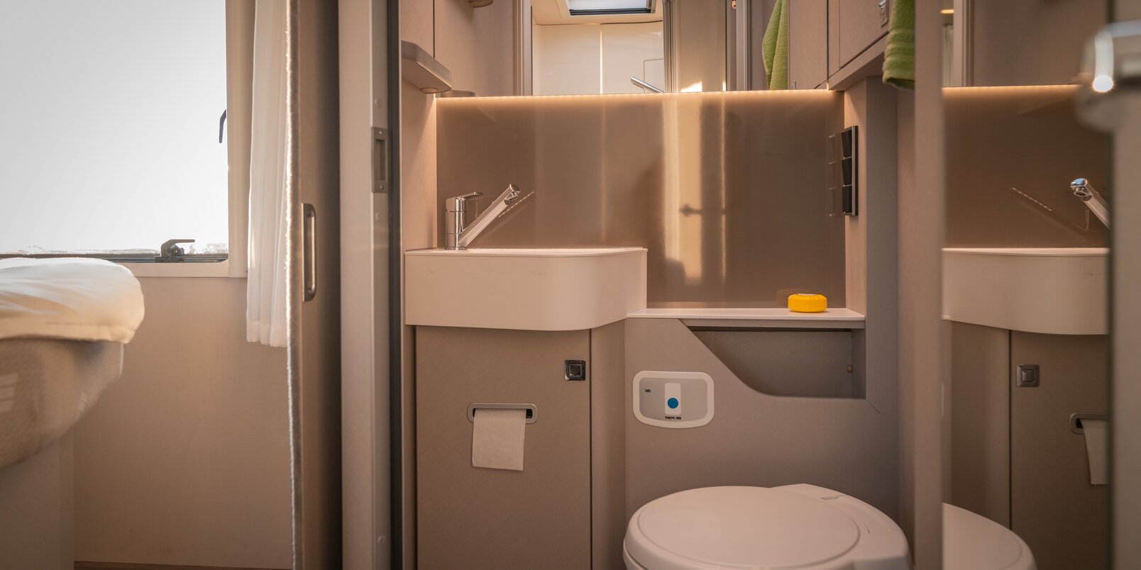 Spiegel, wastafel, opbergruimte en toilet in de badkamer van de HYMER Tramp S camper