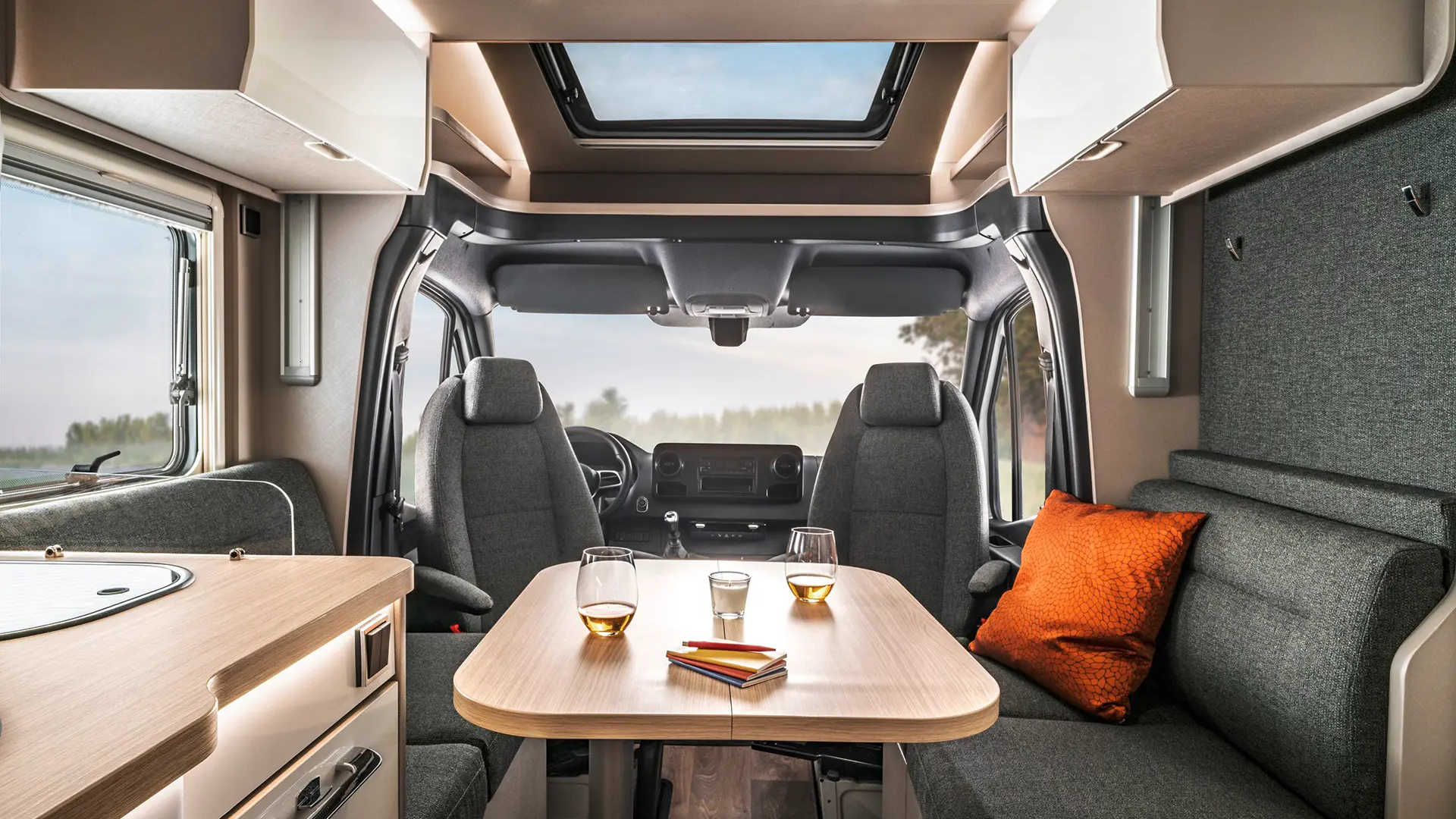 Sitzgruppe mit gedecktem Tisch und Dekokissen und Fahrerhaus mit Fahrersitzen zur Sitzgruppe gedreht im HYMER Tramp S