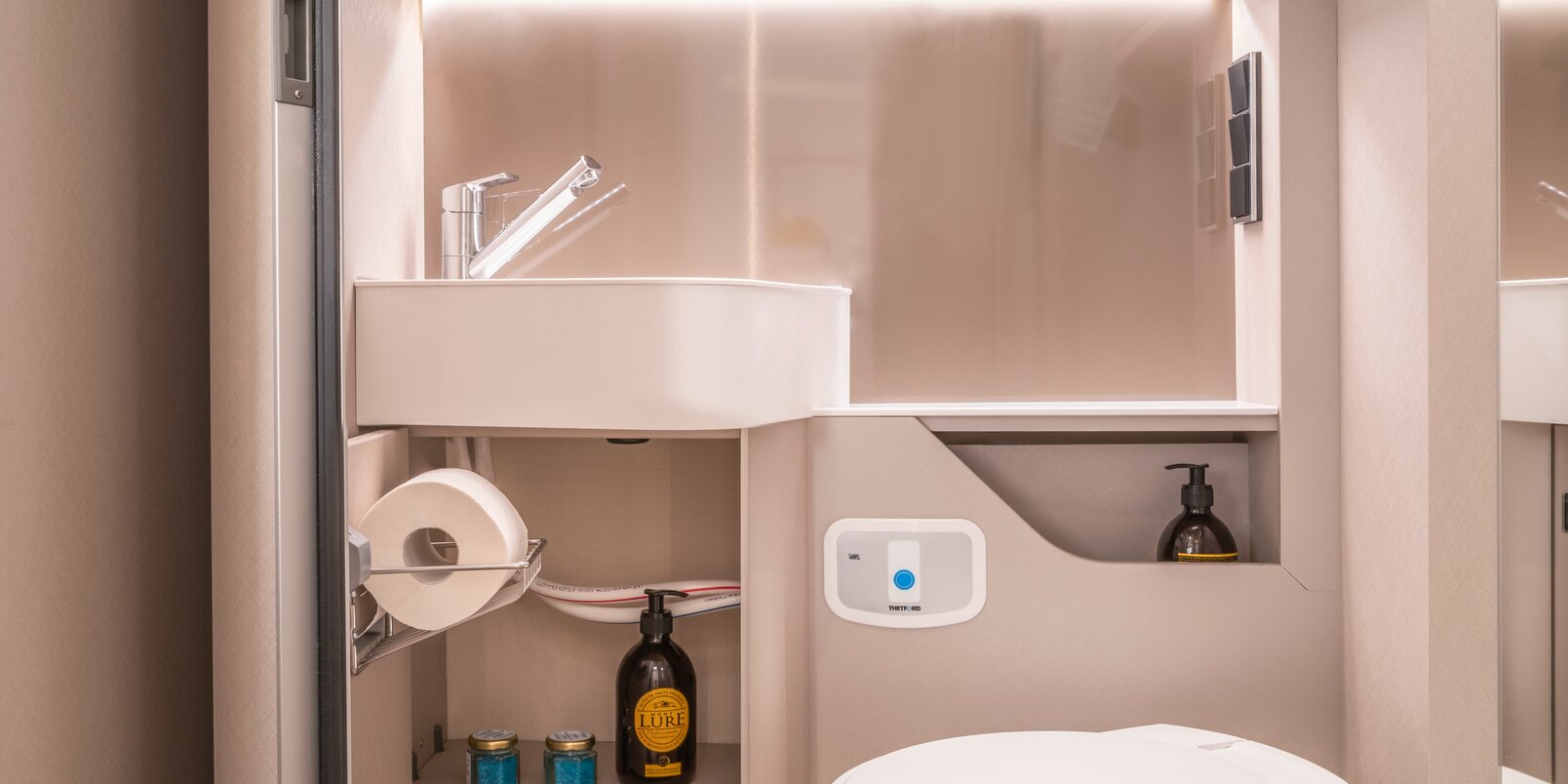 Spiegel, wastafel, toilet en kasten gevuld met badkameraccessoires in de badkamer van de HYMER Tramp S camper