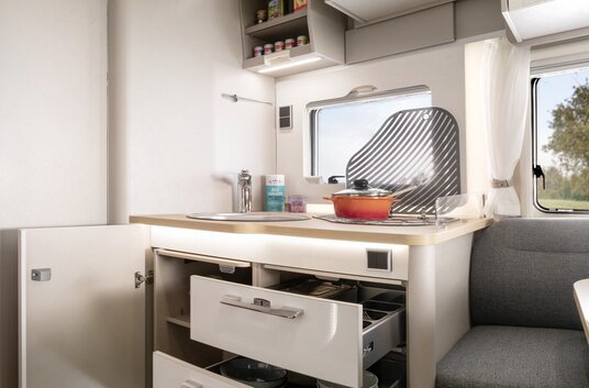 Garderobe, flatscreen, open lades en kasten vol keukenaccessoires in het keukenblok van de HYMER T-Class S