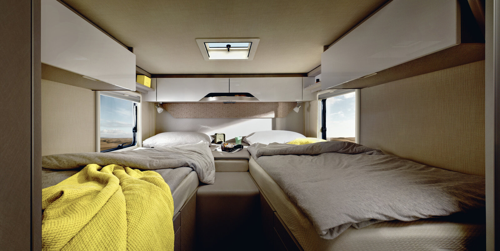 Schlafbereich im HYMER Tramp S 680: zwei bezogene Längseinzelbetten, gelbes Badetuch, mittiger Zugang, Dachstauschränke