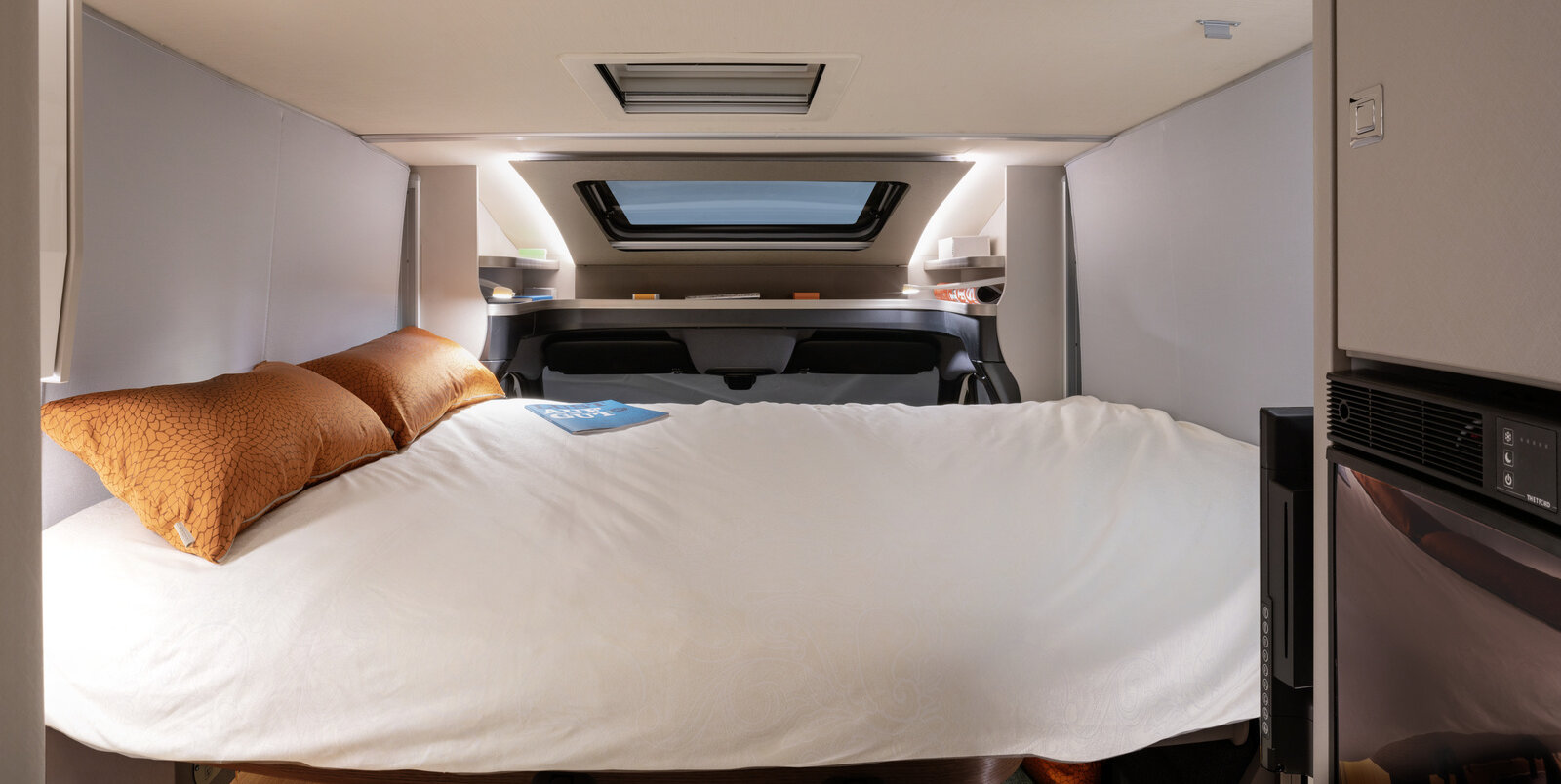 Covered fold-down bed with orange-colored decorative cushions over the seating area, panoramic skylight on the HYMER T-Class S.