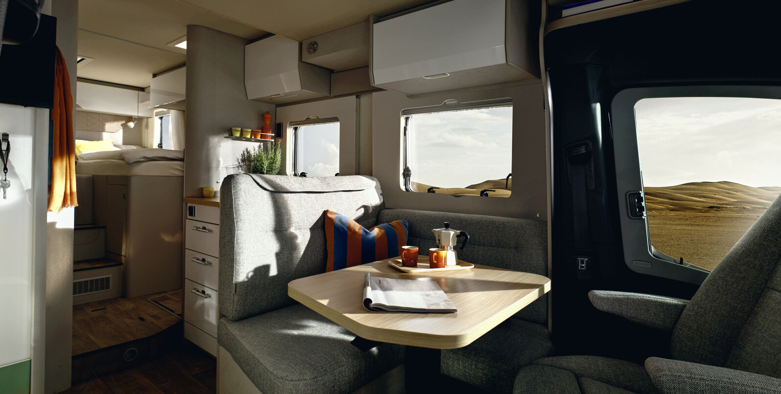 L-Sitzgruppe mit Kissen und gedecktem Tisch, Fahrersitz, Küchenblock und Schlafbereich im HYMER Tramp S 