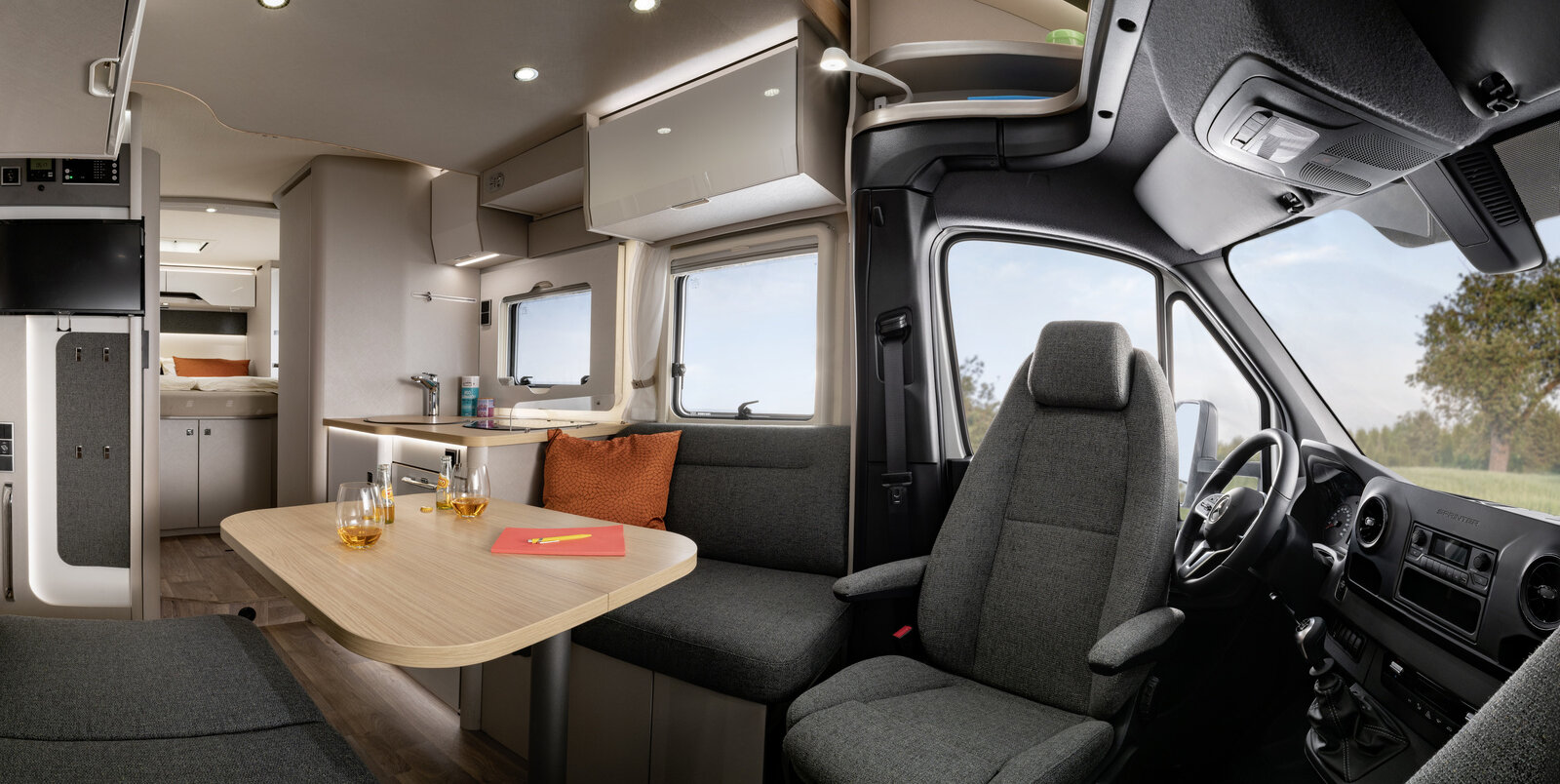 Living room in the HYMER T-Class S 695: driver's cab, seating area with a laid table, kitchen, bathroom and sleeping area