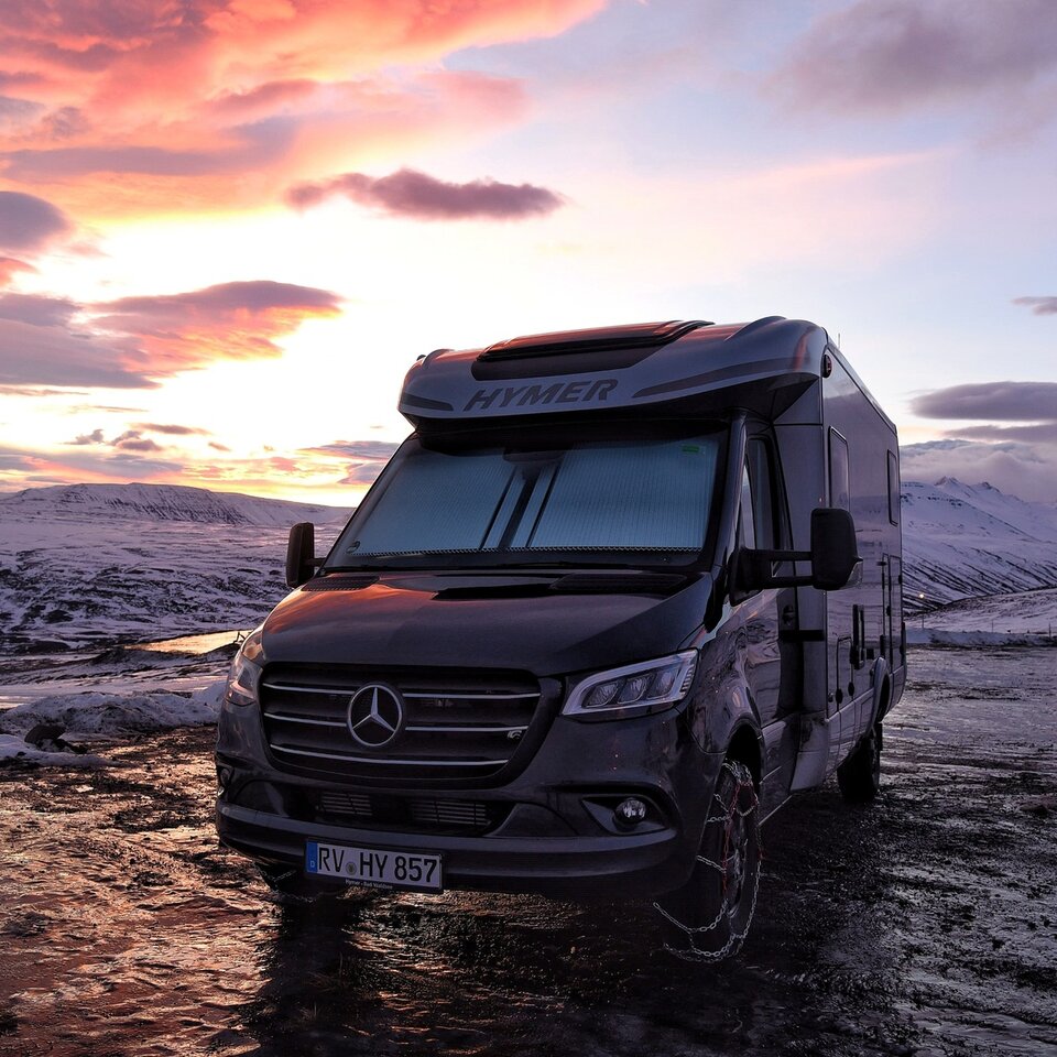 Asuntoauto seisoo auringonlaskussa lumisessa ympäristössä. Kuvattu matkailuautolla tehdyllä matkalla Islantiin lautalla.