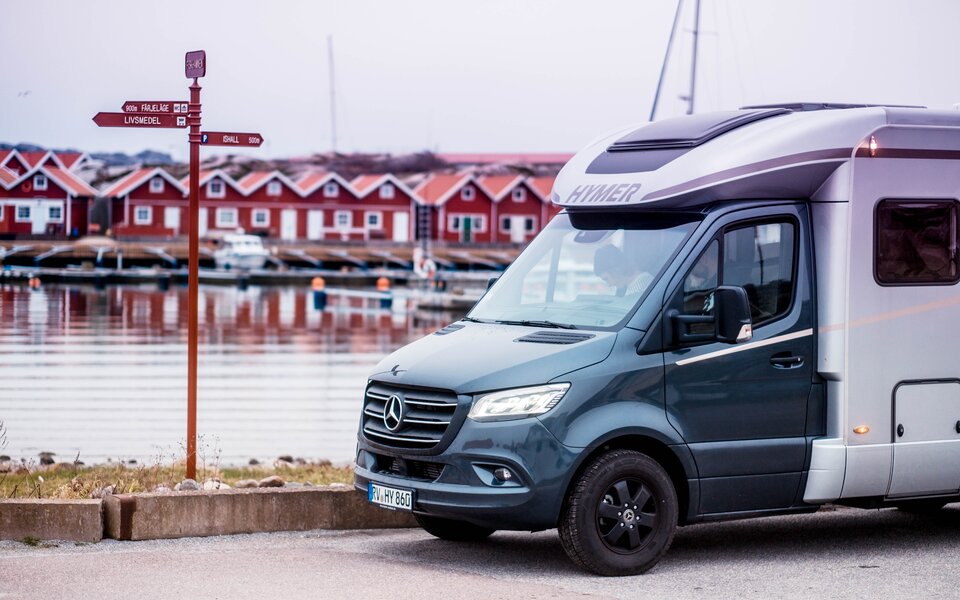 Teilintegriertes Wohnmobil vor schwedischer Schärenlandschaft mit roten Häusern 
