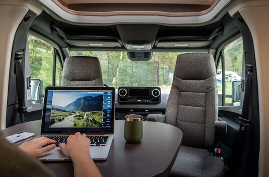 Persoon aan tafel in de zitgroep van een camper en bekijkt landschap foto´s op de laptop