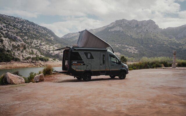 Side view of the passenger side of the Venture S, with the pop-top and Sunset Deck extended, mountains and water in the background.