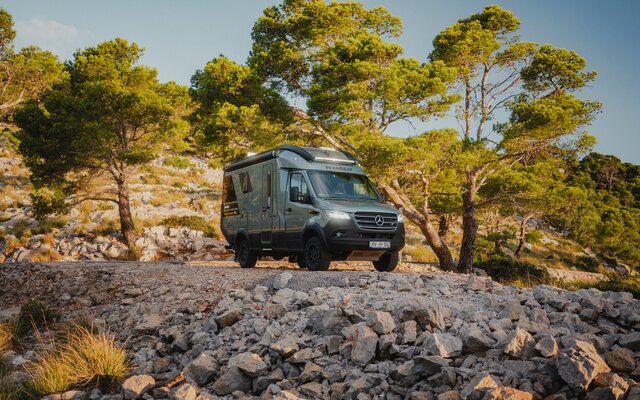 View from the front side of the Venture S, headlights on, standing in front of a rocky abyss, surrounded by trees.