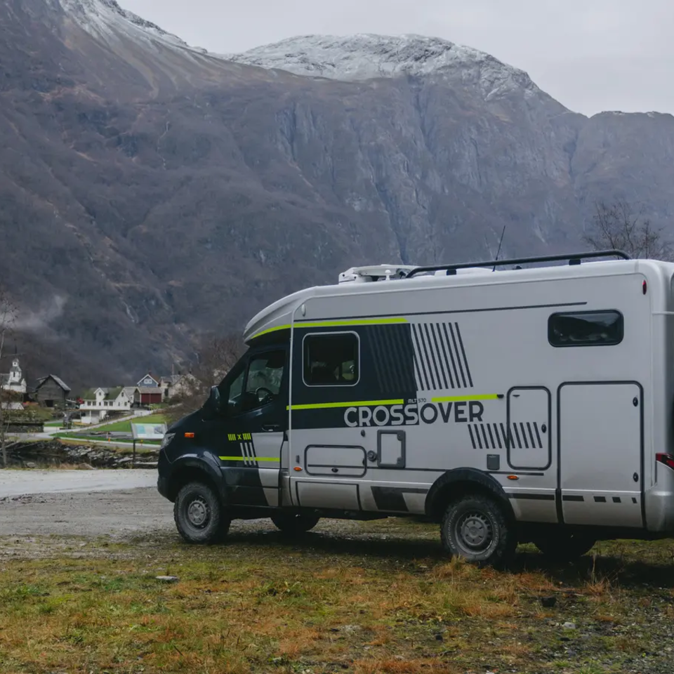 Seitlicher Blick auf die Fahrerseite vom HYMER ML-T CrossOver, das Fahrezug steht auf einem Parkplatz, im Hintergrund sind große Berge mit riesigen Felswänden