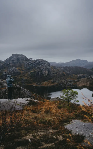 Blick von Hinten auf einen Mann der ein Foto von einem See macht, der See ist umschlossen von einer Felslandschaft