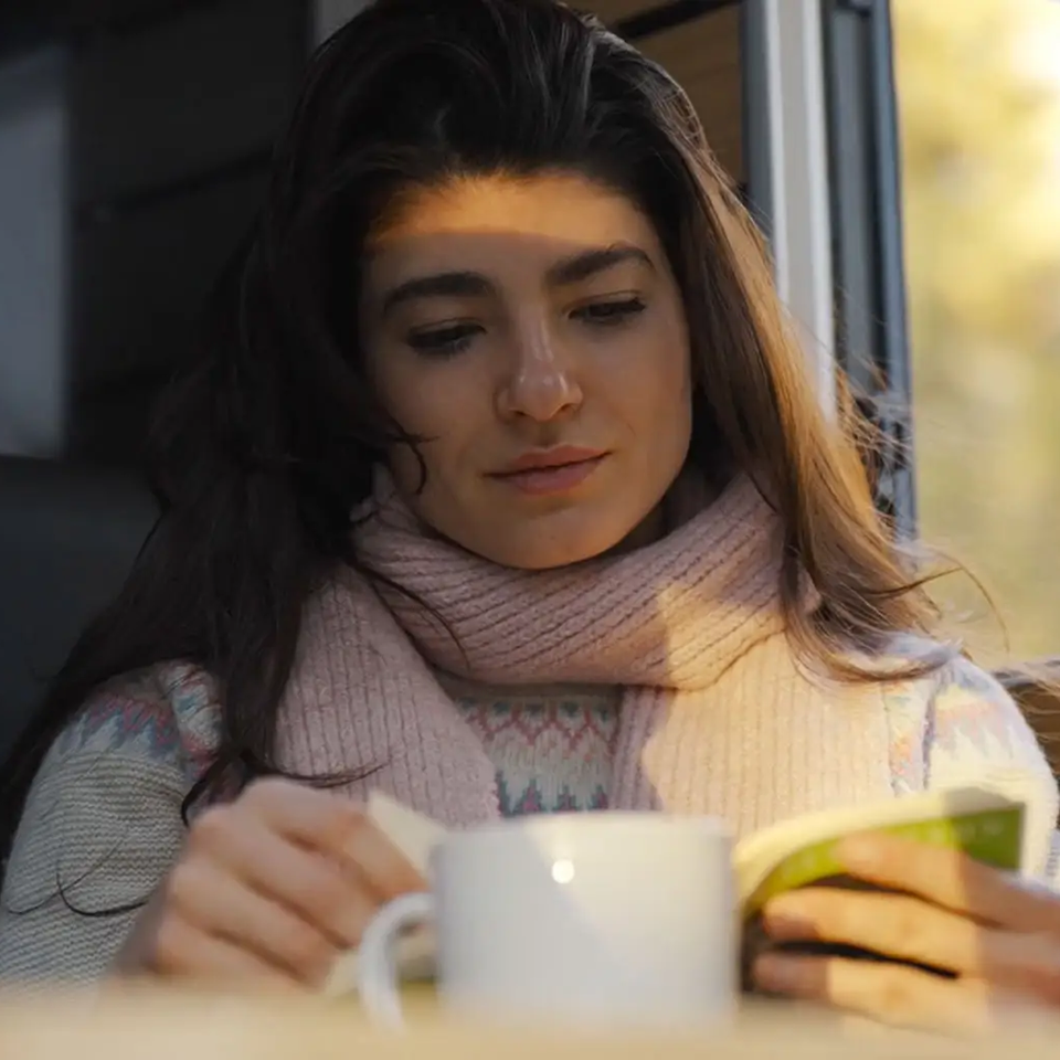 Nahaufnahme einer Frau, die ein Buch liest und eine weiße Kaffeetasse vor sich stehen hat