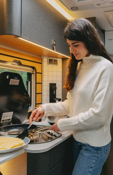 Junge Frau die in einer Wohnmobilküche eines sehr modernen Wohnmobils Pfannkuchen zubereitet