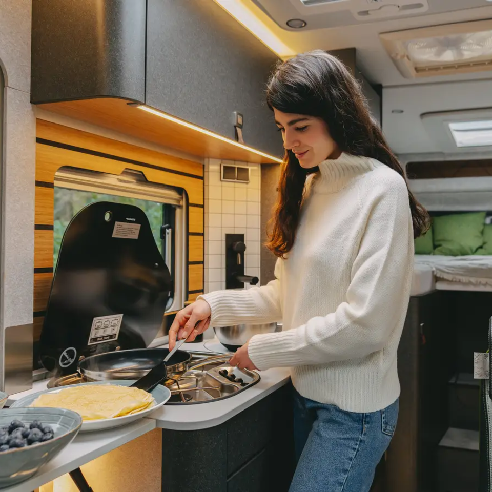 Young woman preparing pancakes in the motorhome kitchen of a very modern motorhome