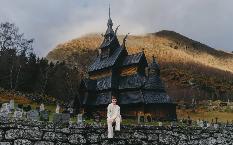 Blick auf eine Frau die auf einer Steinmauer sitzt, im Hintergrund ist die Borgund Stabkirche
