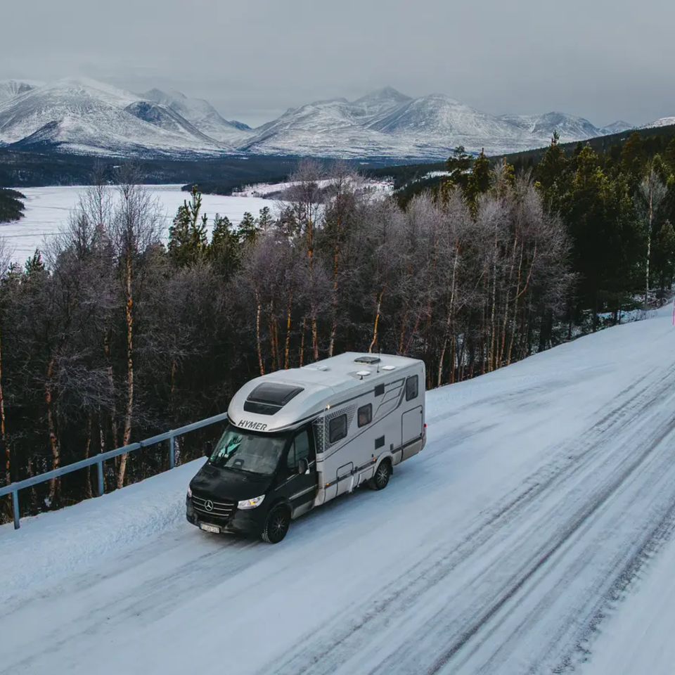 Blick auf den HYMER B-MC, Er parkt auf einer verschneiten Straße, im Hintergrund sind Schneeberge.