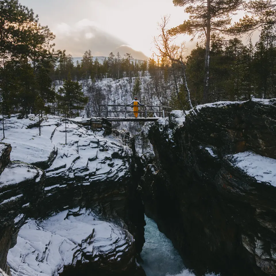 Blick auf eine Schlucht mit einem Wasserfall, im Mittelpunkt ist eine Person auf einer Brücke über der Schlucht