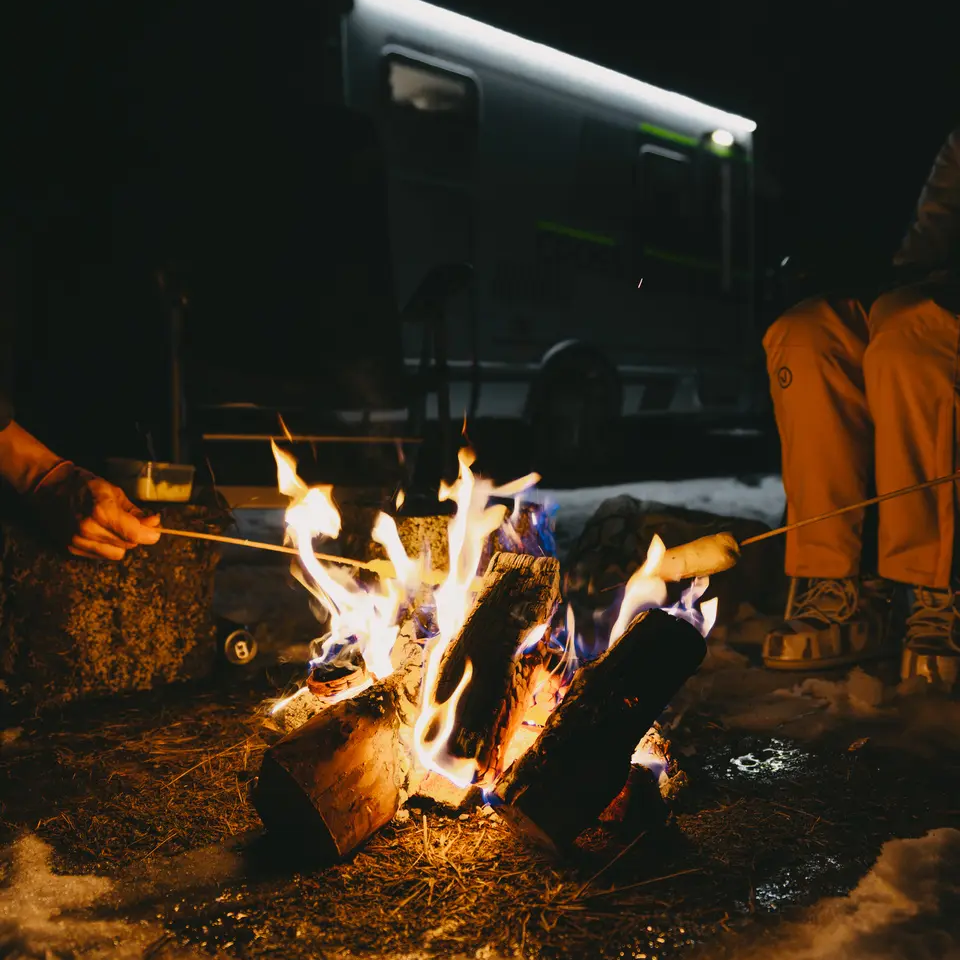 Blick auf ein Lagerfeuer, es werden Marshmallows gegrilt, im Hintergrund ist der HYMER ML-T CrossOver zu sehen