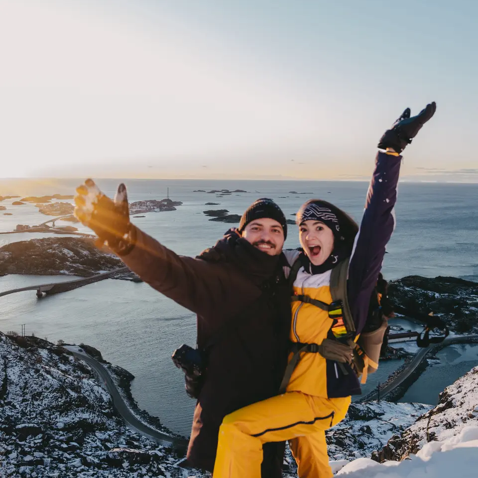 Mann und Frau an einem Aussichtspunkt, im Hintergrund sind verschneite Berge und das Meer