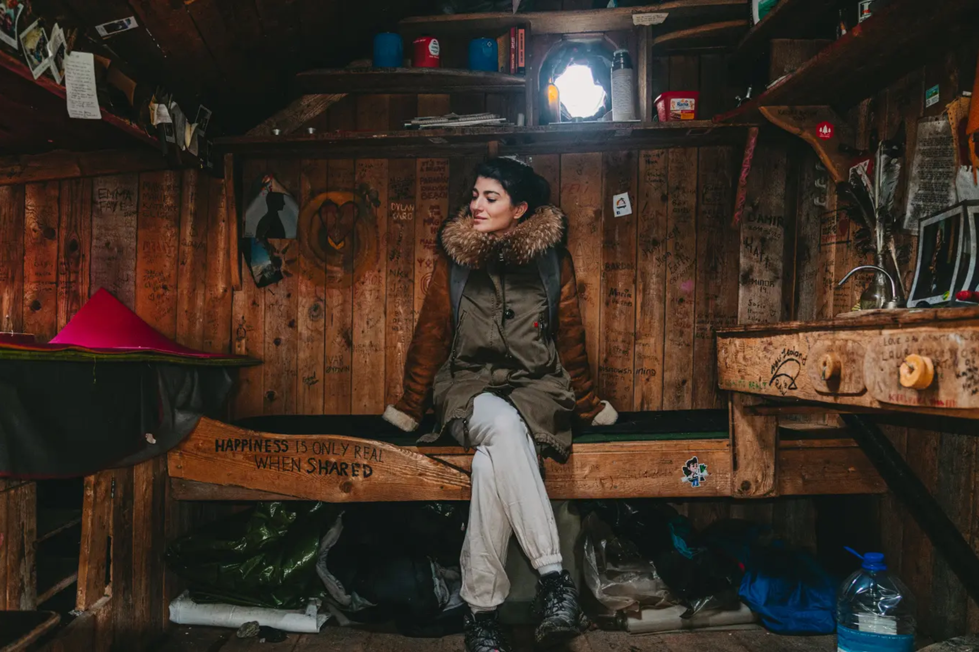 Eine Frau sitzt in einer Holzhütte mit vielen Utensilien im Raum