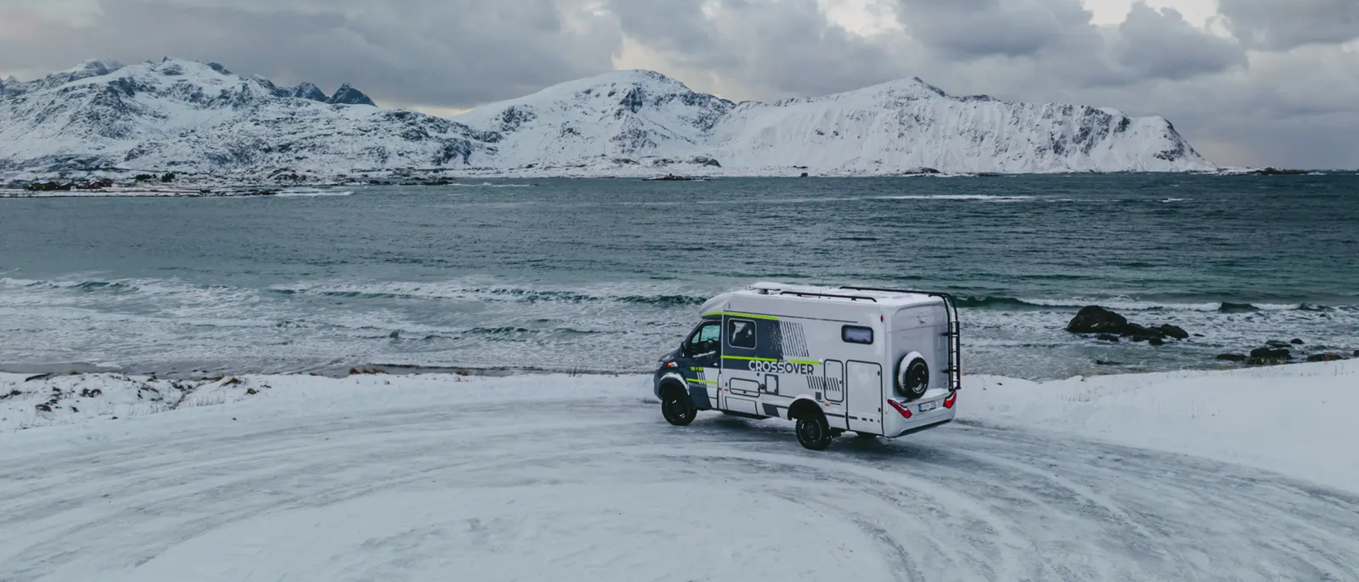 HYMER ML-T 570 CrossOver parkt an einem Aussichtspunkt, im Hintergrund ist das Meer und verschneite Berge
