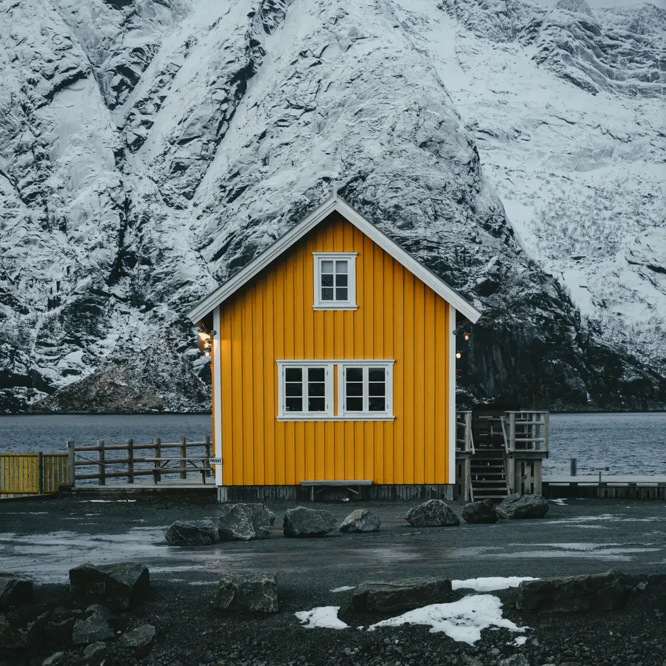 Gelbes kleines Haus am Fjord, im Hintergrund ist ein großer Berg mit Schnee