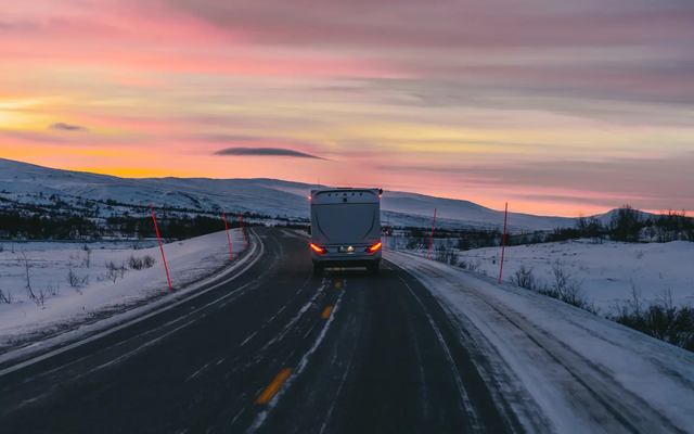 HYMER B-MC T BlackLine fährt auf einer Straße, Blick von hinten, im Hintergrund ist ein schöner Sonnenuntergang