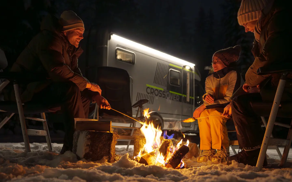 3 Leute sitzen am Lagerfeuer und machen Stockbrot, im Hintergrund ist der HYMER ML-T 570 CrossOver
