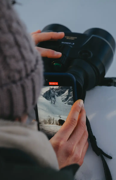 Frau filmt mit ihrem Handy durch ein Fernglas