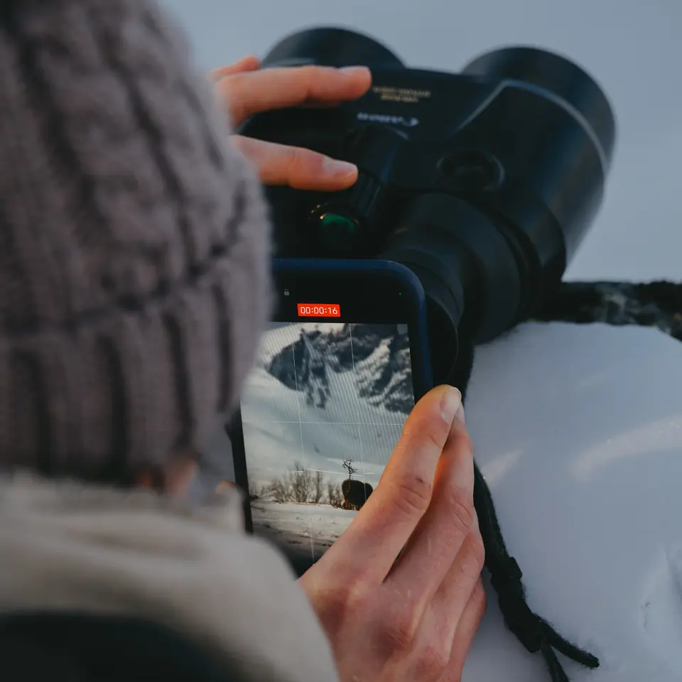 Woman filming with her phone through binoculars