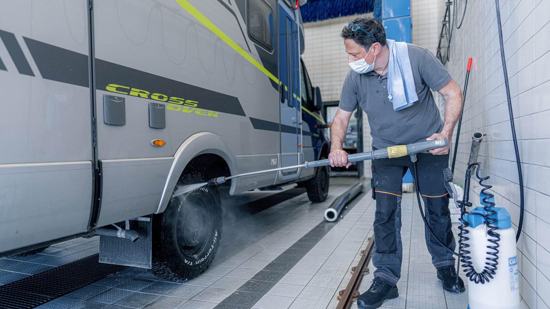 HYMER owner using a jet wash to thoroughly clean the HYMER CrossOver's studded tires in the wash hall.
