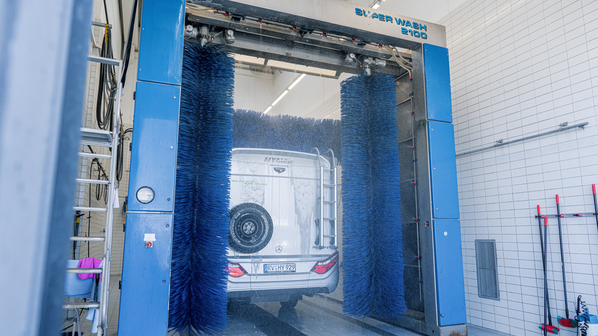 Vista posterior de la autocaravana HYMER con rueda de repuesto en el panel posterior sécandose en los rodillos de secado del túnel de lavado