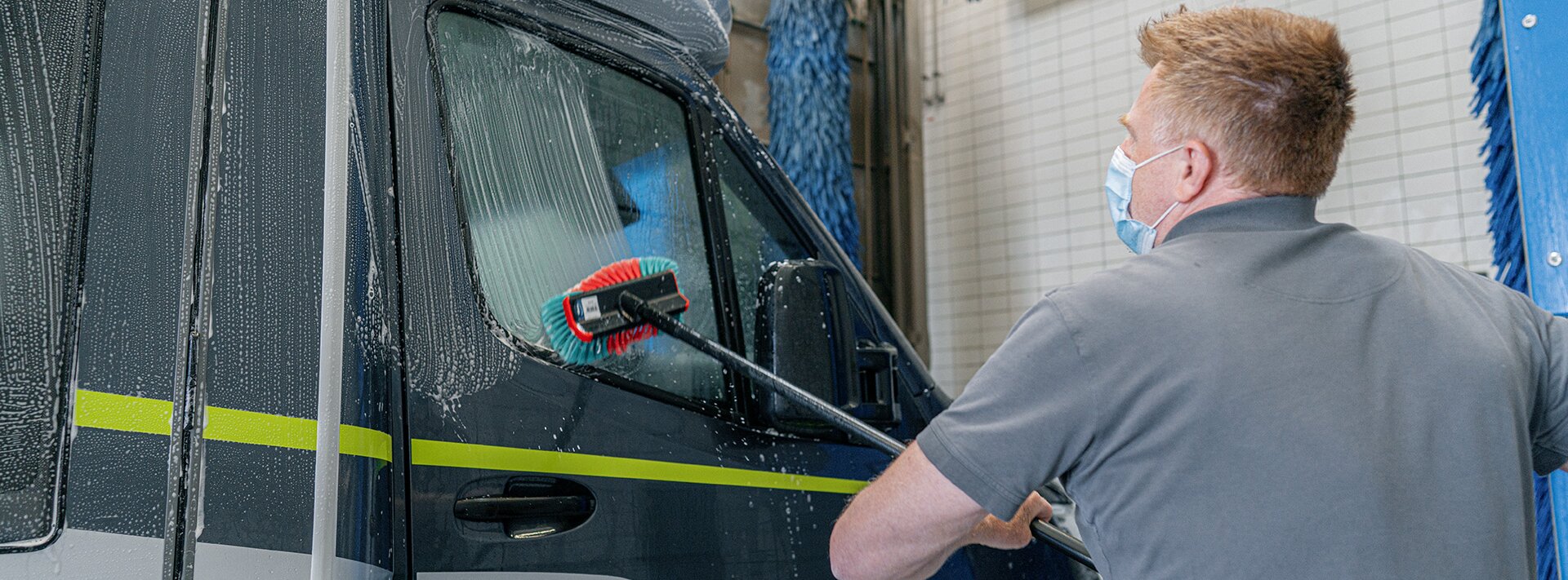Propietario de un HYMER limpiando su autocaravana HYMER CrossOver con un cepillo de lavado enjabonado en la zona de lavado